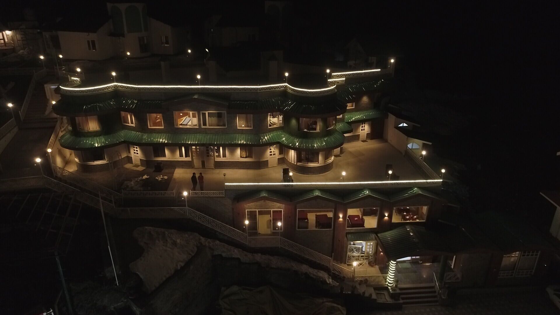 A multi-story building with a curved roofline and multiple balconies, illuminated by exterior lighting.