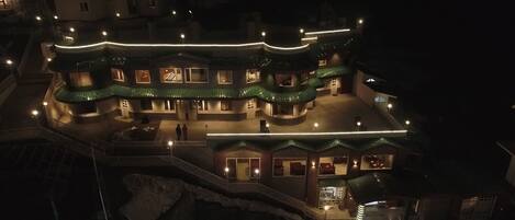 A multi-story building with a curved roofline and multiple balconies, illuminated by exterior lighting.
