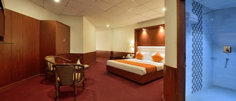 Une chambre d’hôtel avec un lit, un bureau et une chaise. Elle comprend une salle de bain avec une douche et des toilettes.
