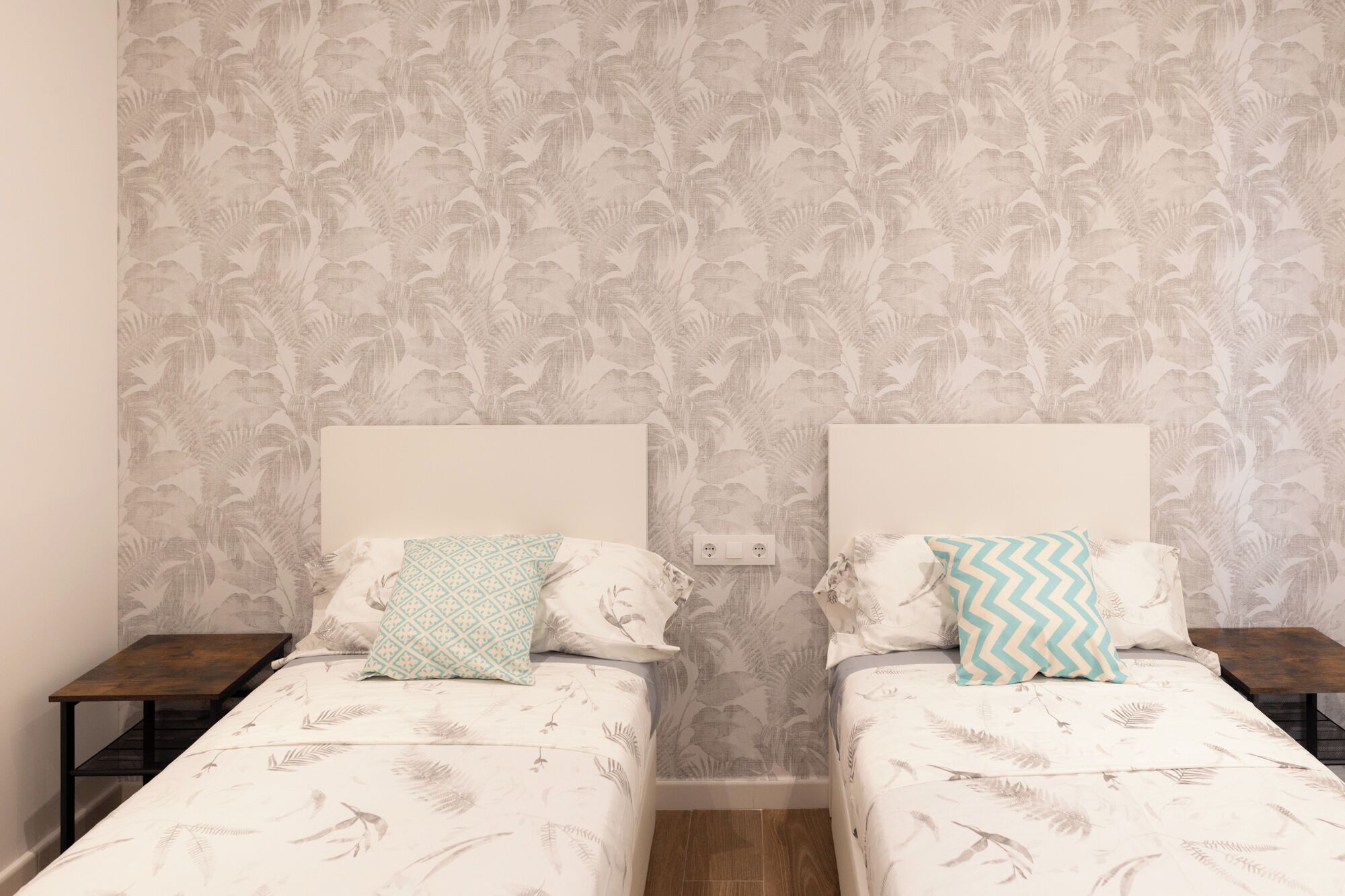Una habitación con dos camas, cada una con una colcha estampada y almohadas a juego. Hay dos mesitas de noche, una a cada lado de las camas.