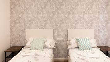 Una habitación con dos camas, cada una con una colcha estampada y almohadas a juego. Hay dos mesitas de noche, una a cada lado de las camas.