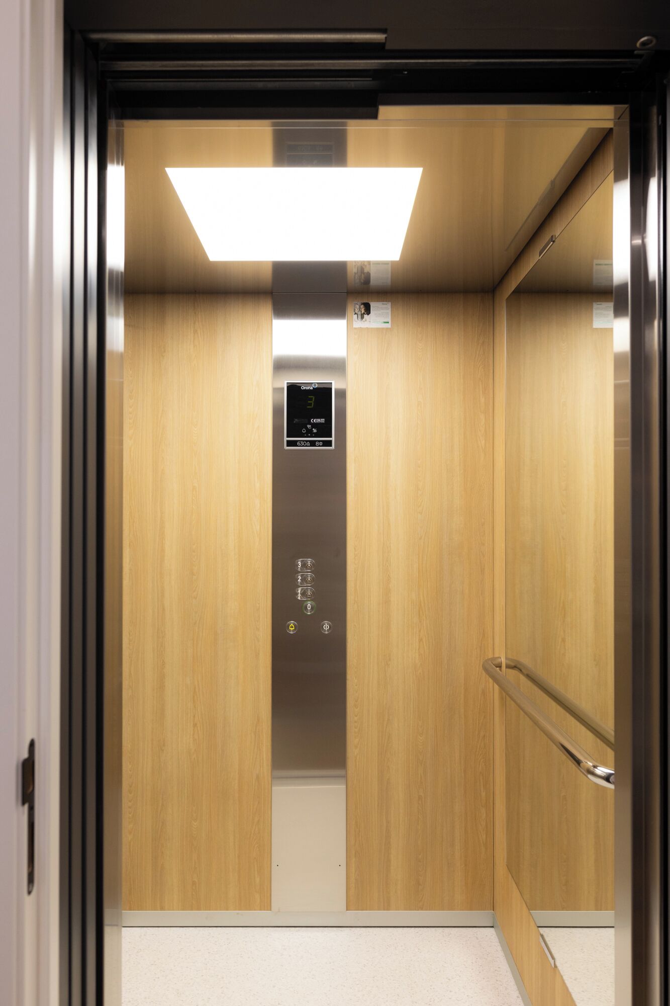 Een lift met een houten interieur, een digitaal display en een handgreep.