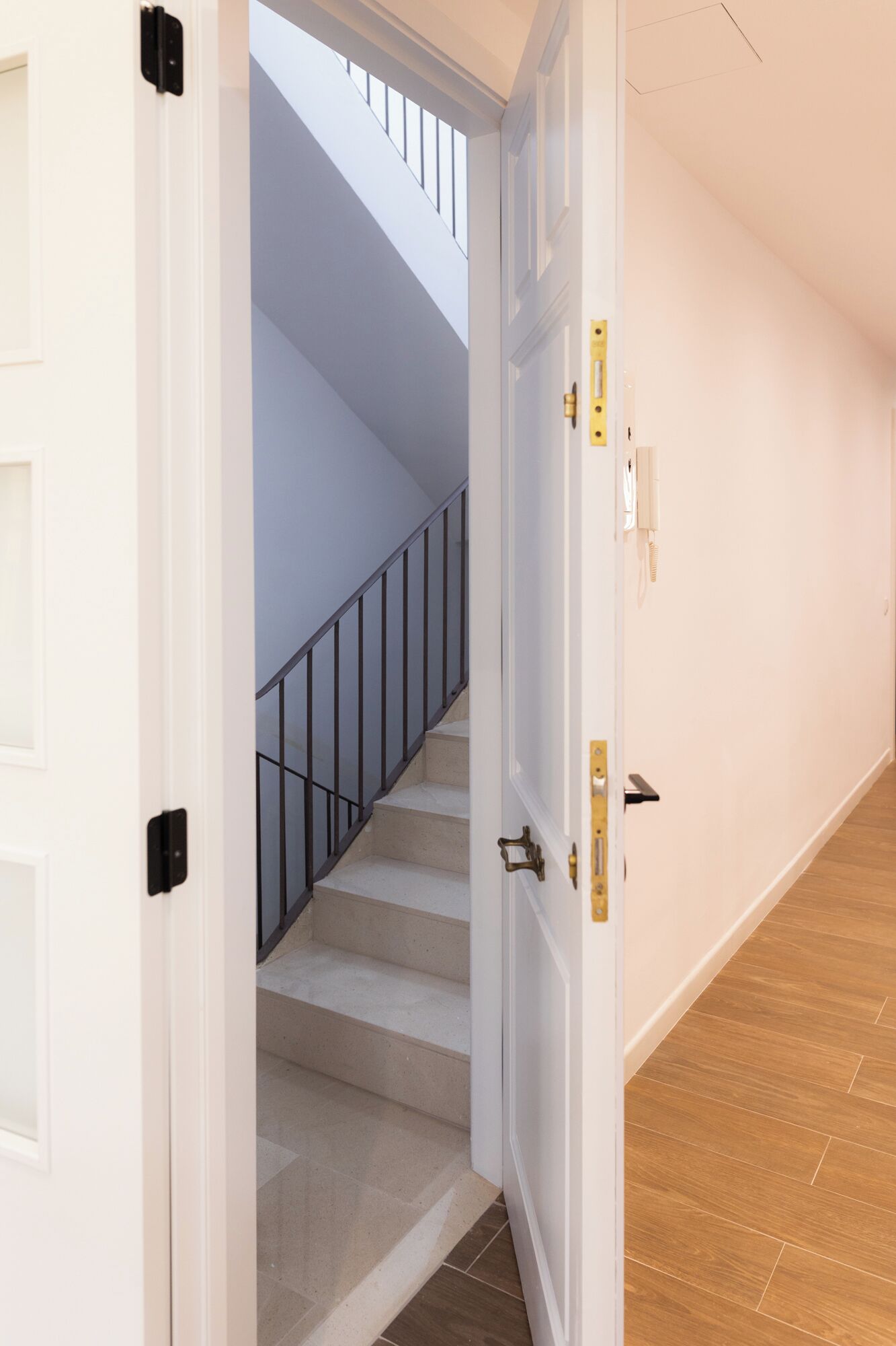 A hallway with a wooden floor leading to a staircase with a glass railing.