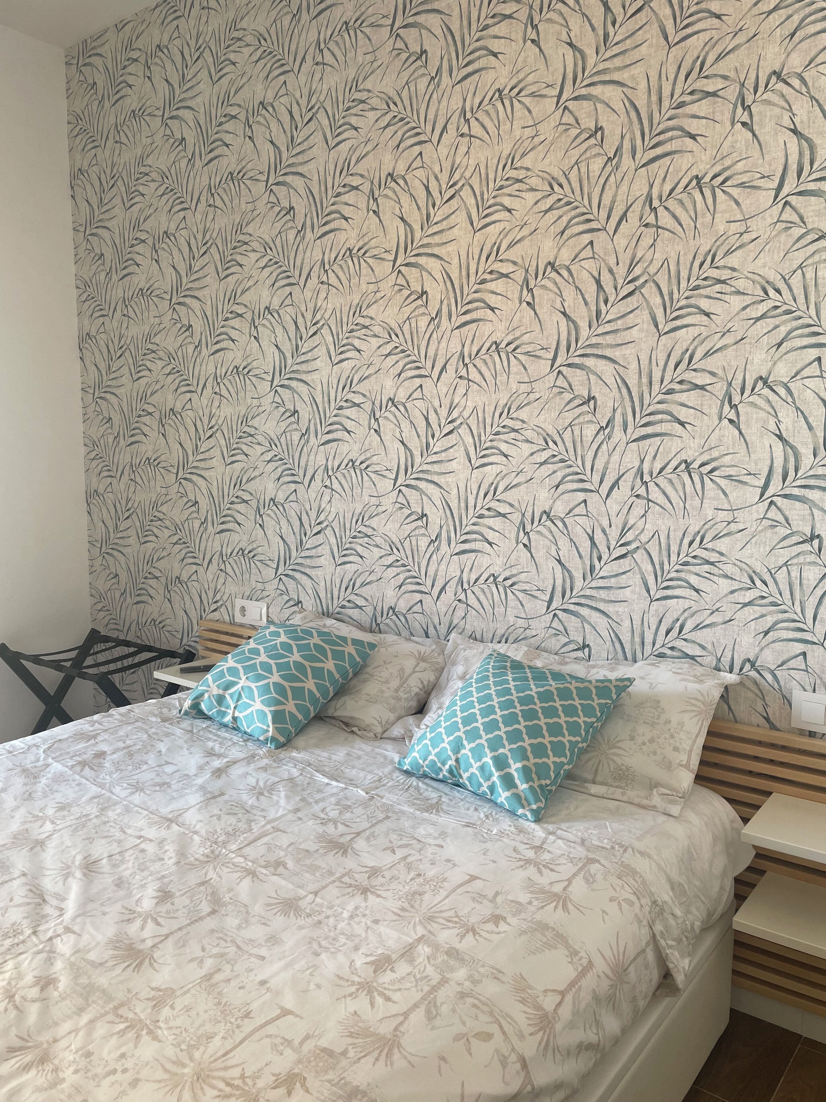 Un dormitorio con papel tapiz estampado, una cama con ropa de cama floral y dos almohadas.