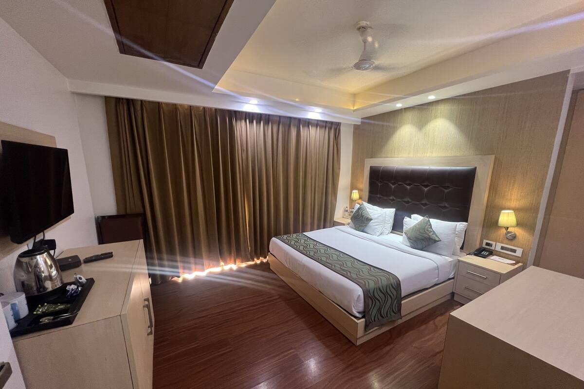 Habitación de hotel con cama, mesitas de noche, televisión, cortinas y ventilador de techo.
