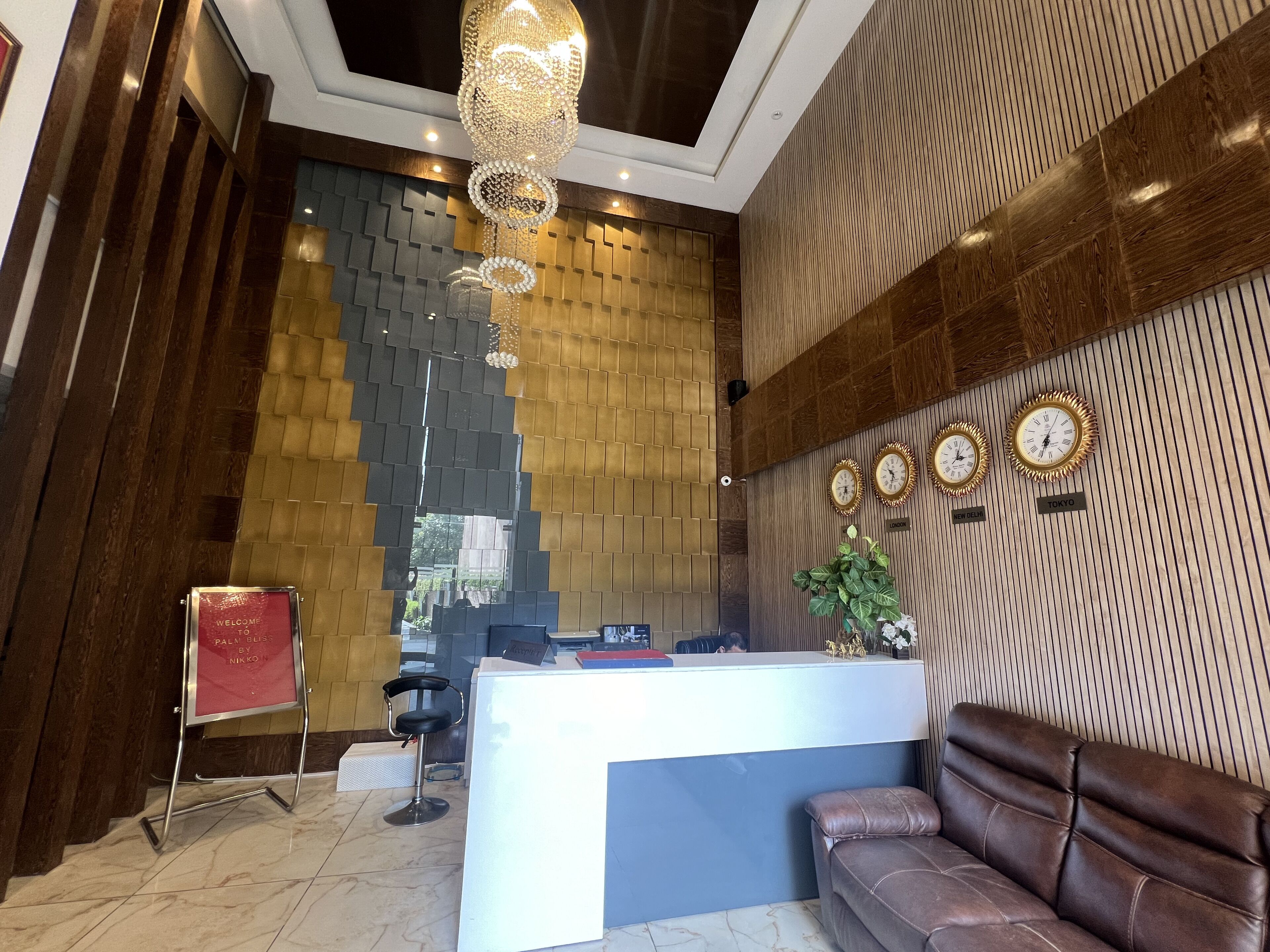 A reception area with a modern design, featuring a reception desk, a brown leather sofa, and a decorative wall with clocks and a plant.