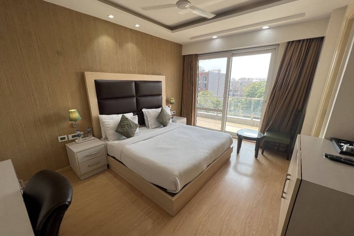 Habitación de hotel con una cama grande, un escritorio, una silla, una mesita y vistas a la ciudad a través de la ventana.