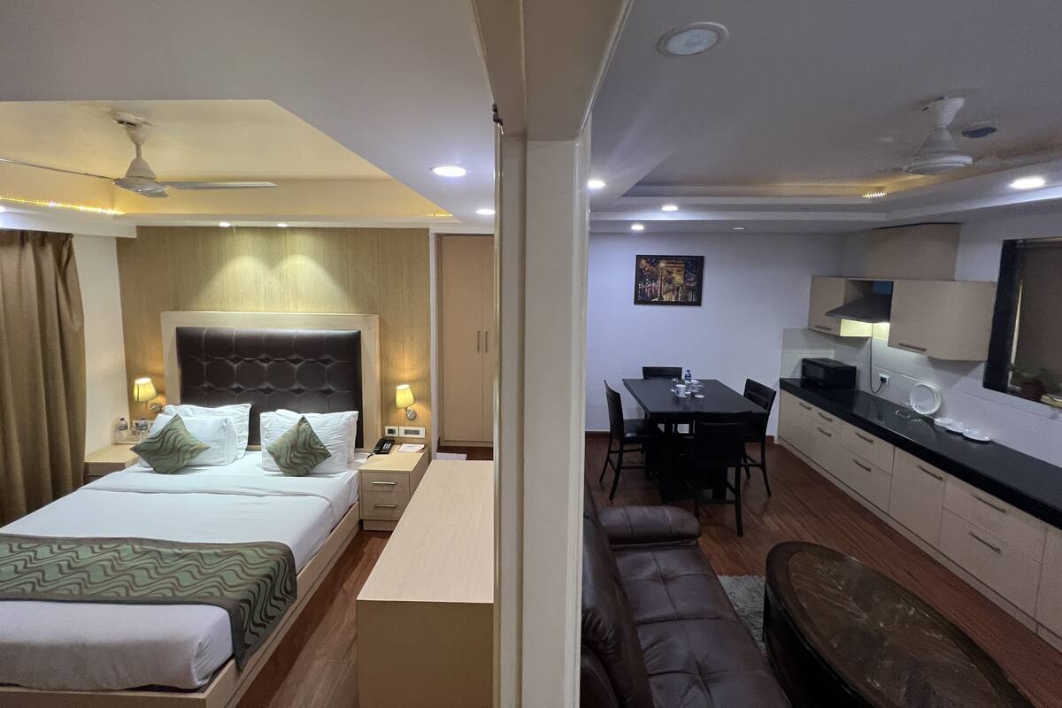 Habitación de hotel con cama, mesitas de noche, escritorio, sofá, mesa de comedor y zona de cocina.