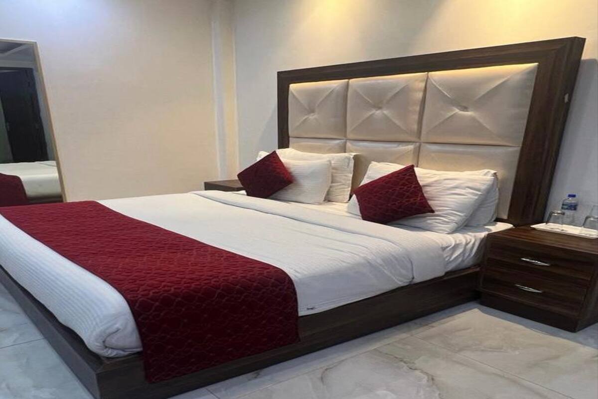 Una cama bien hecha con una colcha roja, un cabecero de madera y una mesita de noche con una lámpara.