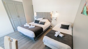 Habitación de hotel con dos camas, suelo de madera, un armario y una silla.