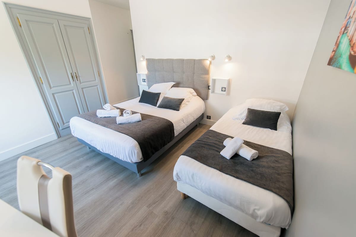 Quarto de hotel com duas camas, soalho de madeira, um guarda-roupa e uma cadeira.