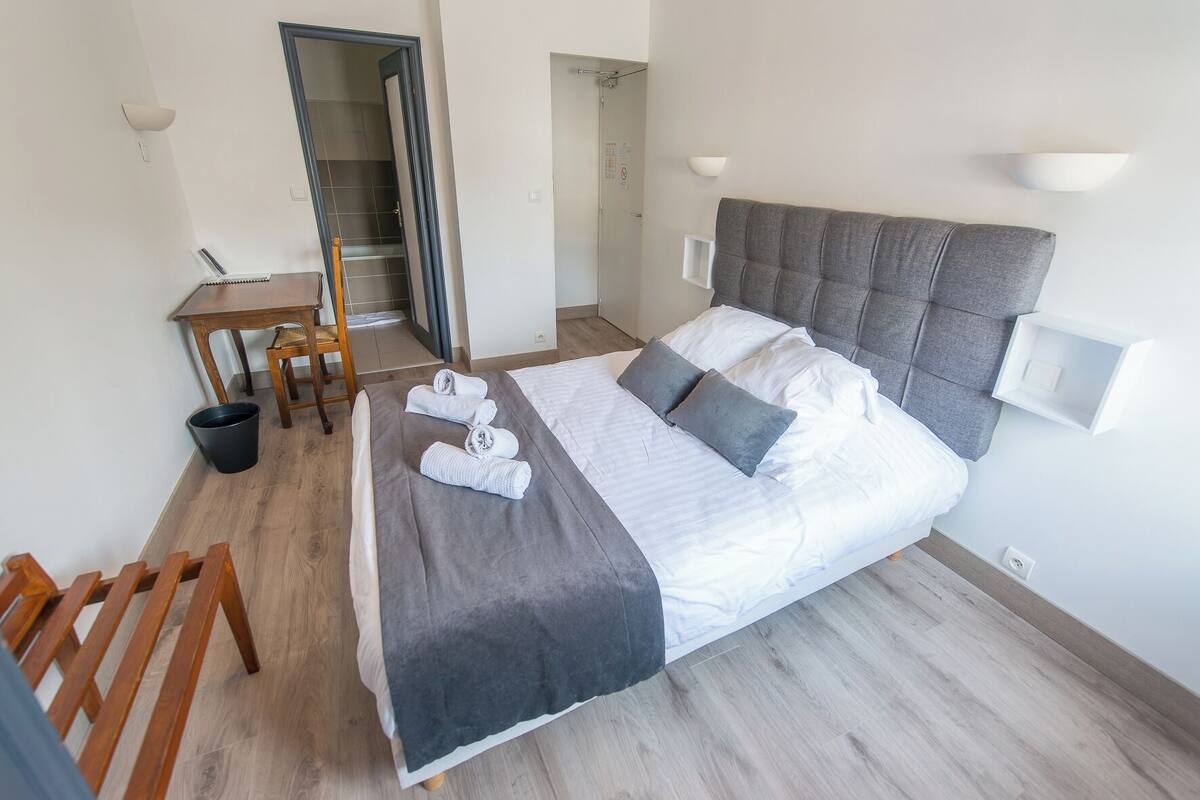 Quarto de hotel bem arrumado, com cama, escrivaninha e cadeira.