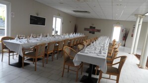 Un comedor con largas mesas dispuestas para una comida, sillas de madera y un piso de baldosas blancas.