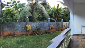 Un balcon donnant sur un jardin, un mur blanc et une fenêtre avec des stores.