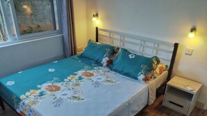 Un lit avec une literie à motifs floraux, deux tables de chevet et des lampes fixées au mur.
