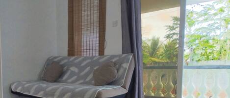A modern room with a sofa, a large window, and a balcony with plants.