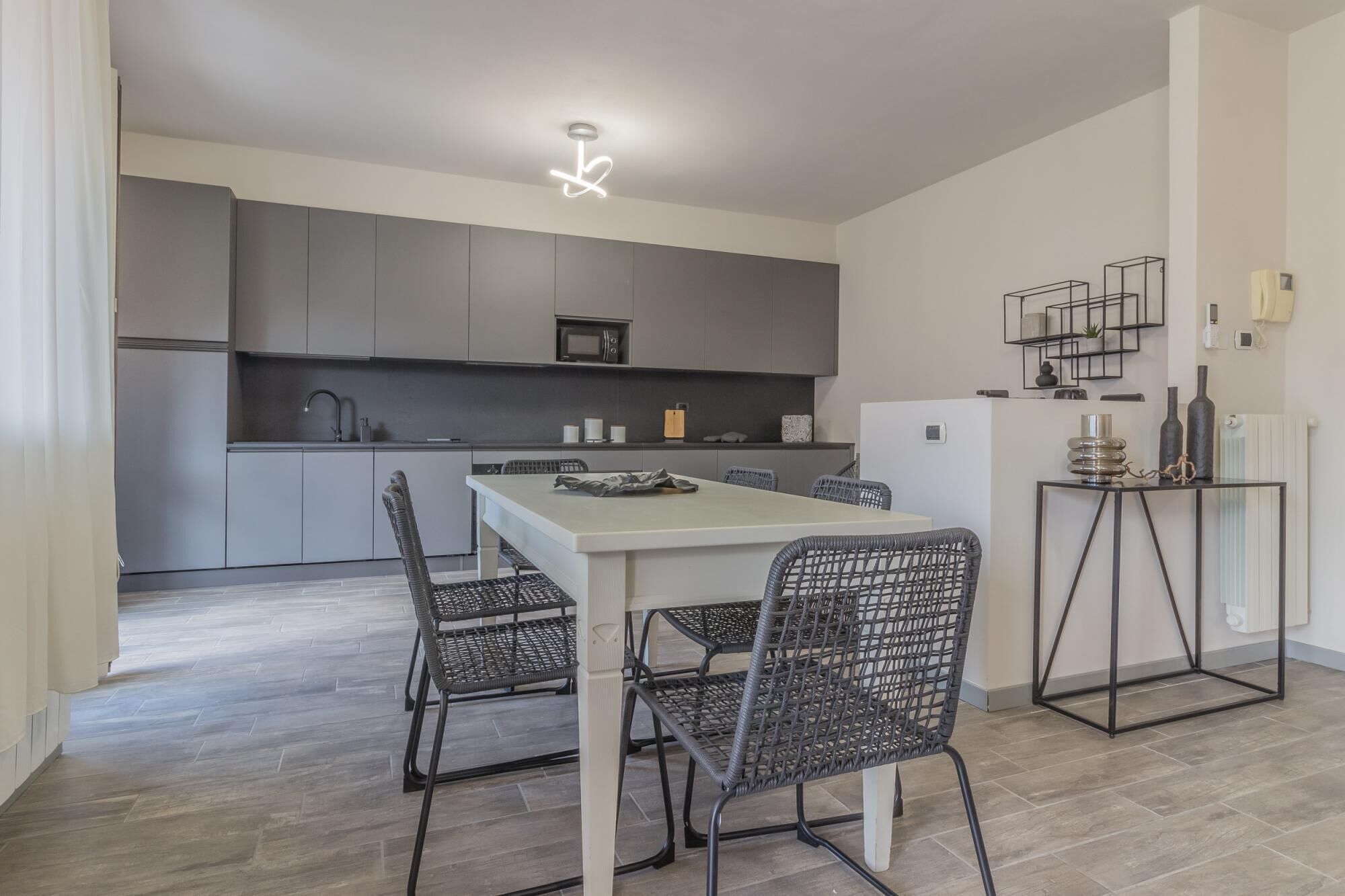Een moderne keuken met grijze kastjes, een witte eettafel en zwarte rieten stoelen.