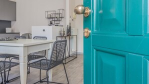 A teal door with a brass doorknob, a white dining table with black chairs, and a kitchen area in the background. - Casa Mimosa in Lierna (Lierna)