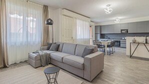 A modern living room with a grey sofa, a small round table, and a dining area with chairs. - Casa Mimosa in Lierna (Lierna)