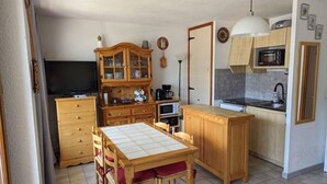Una cocina compacta con comedor, armarios de madera, un microondas y un televisor.