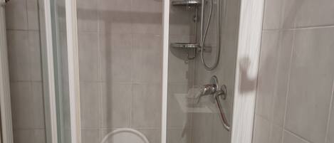 A glass-enclosed shower stall with a built-in seat, a handheld showerhead, and a handheld showerhead mounted on the wall.