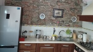 A kitchen with a stone wall, wooden cabinets, a refrigerator, a sink, and a stove. - Historic home in the heart of the medieval village of Avigliana (Avigliana)
