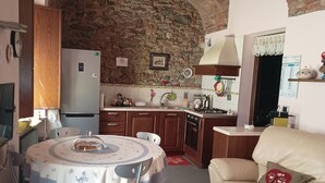 A cozy kitchen with a stone arch ceiling, a dining table with a floral tablecloth, and a beige sofa with a decorative pillow. - Historic home in the heart of the medieval village of Avigliana (Avigliana)