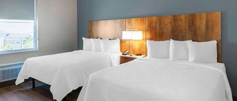 A hotel room with two beds, a nightstand, a lamp, and a window with a view.