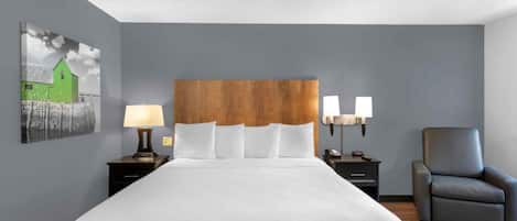 A hotel room with a large bed, a wooden headboard, two bedside lamps, a chair, and a painting on the wall.