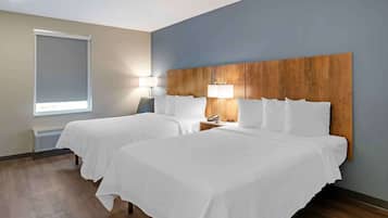 Une chambre d’hôtel avec deux lits, une tête de lit en bois, une fenêtre avec un store et une lampe de chevet.
