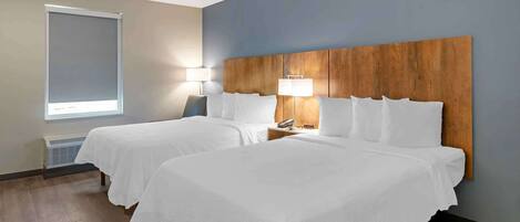 A hotel room with two beds, a wooden headboard, a window with a blind, and a bedside lamp.