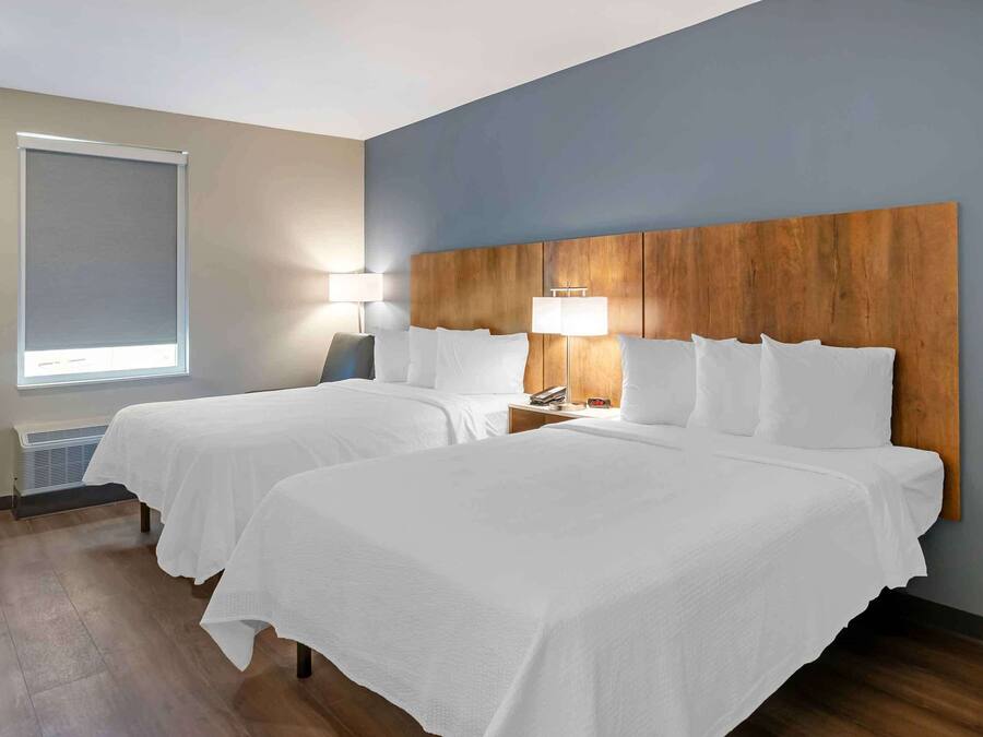 Une chambre d’hôtel avec deux lits, une tête de lit en bois, une fenêtre avec un store et une lampe de chevet.