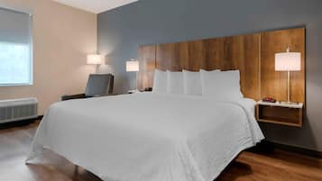 A hotel room with a large bed, a desk, two bedside lamps, and a wall-mounted shelf with a phone and a clock.