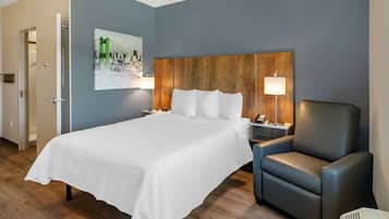 A hotel room with a large bed, a wooden headboard, a nightstand, a lamp, a chair, and a painting of a bridge on the wall.