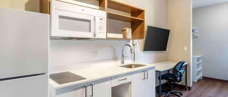 A compact kitchen with white cabinets, a microwave, a sink, and a small workspace with a chair.