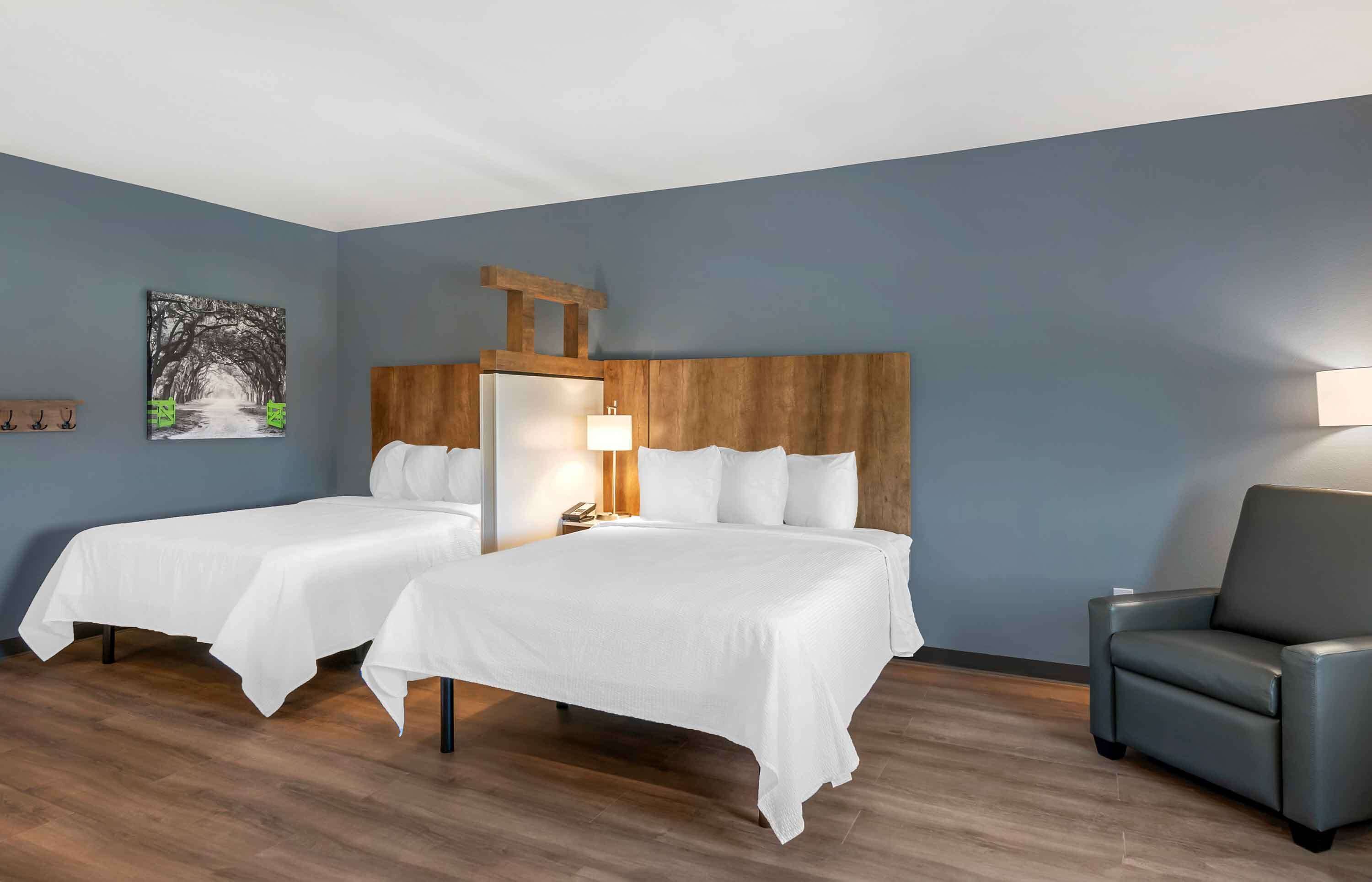 Habitación de hotel con dos camas individuales, un cabecero de madera, un escritorio con una silla y un cuadro en la pared.