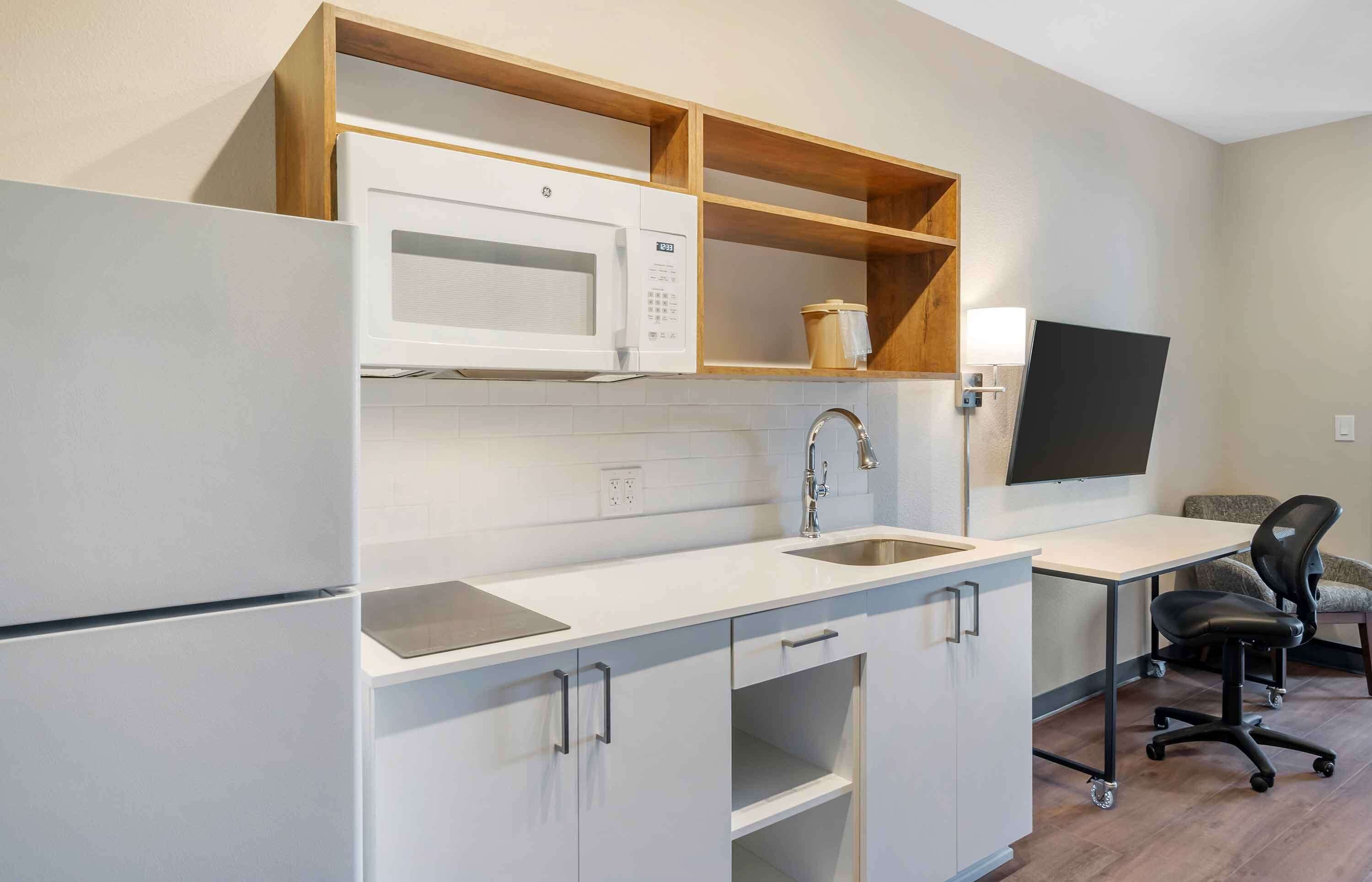 A compact kitchen with a microwave, sink, and wooden shelves.
