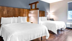 Hotelkamer met twee bedden, houten hoofdborden, wit beddengoed, een nachtkastje, een lamp en een raam met uitzicht.