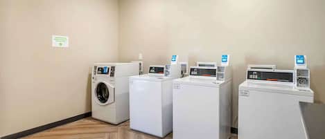 A laundry room with four washing machines, a sign indicating laundry products, and a wooden floor.