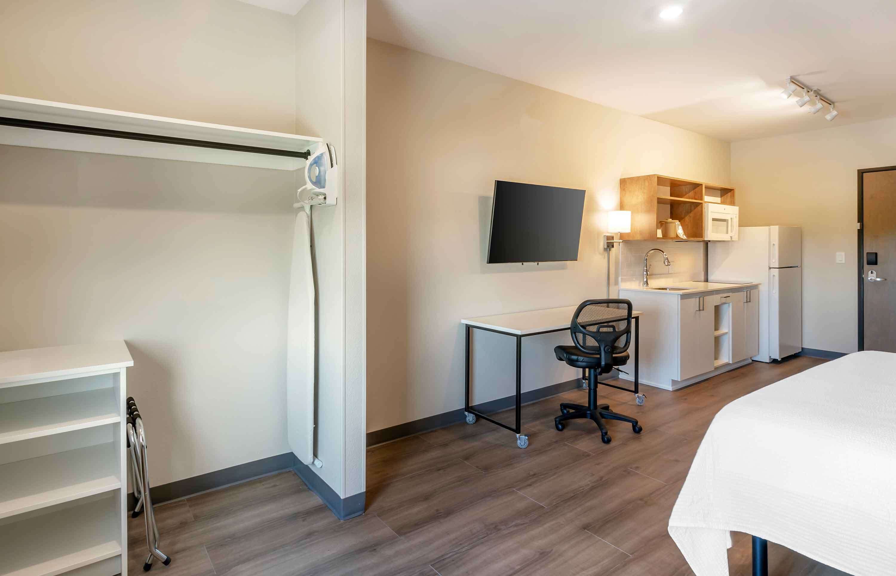 A modern hotel room with a bed, a desk with a chair, a flat-screen TV, a microwave, and a refrigerator.