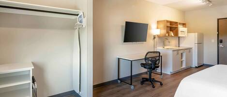 A modern hotel room with a bed, a desk with a chair, a flat-screen TV, a microwave, and a refrigerator.