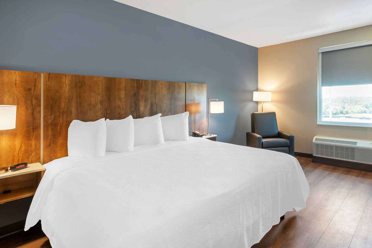 Een hotelkamer met een groot bed, een houten hoofdbord, een bureau met lamp, een stoel en een raam met uitzicht.