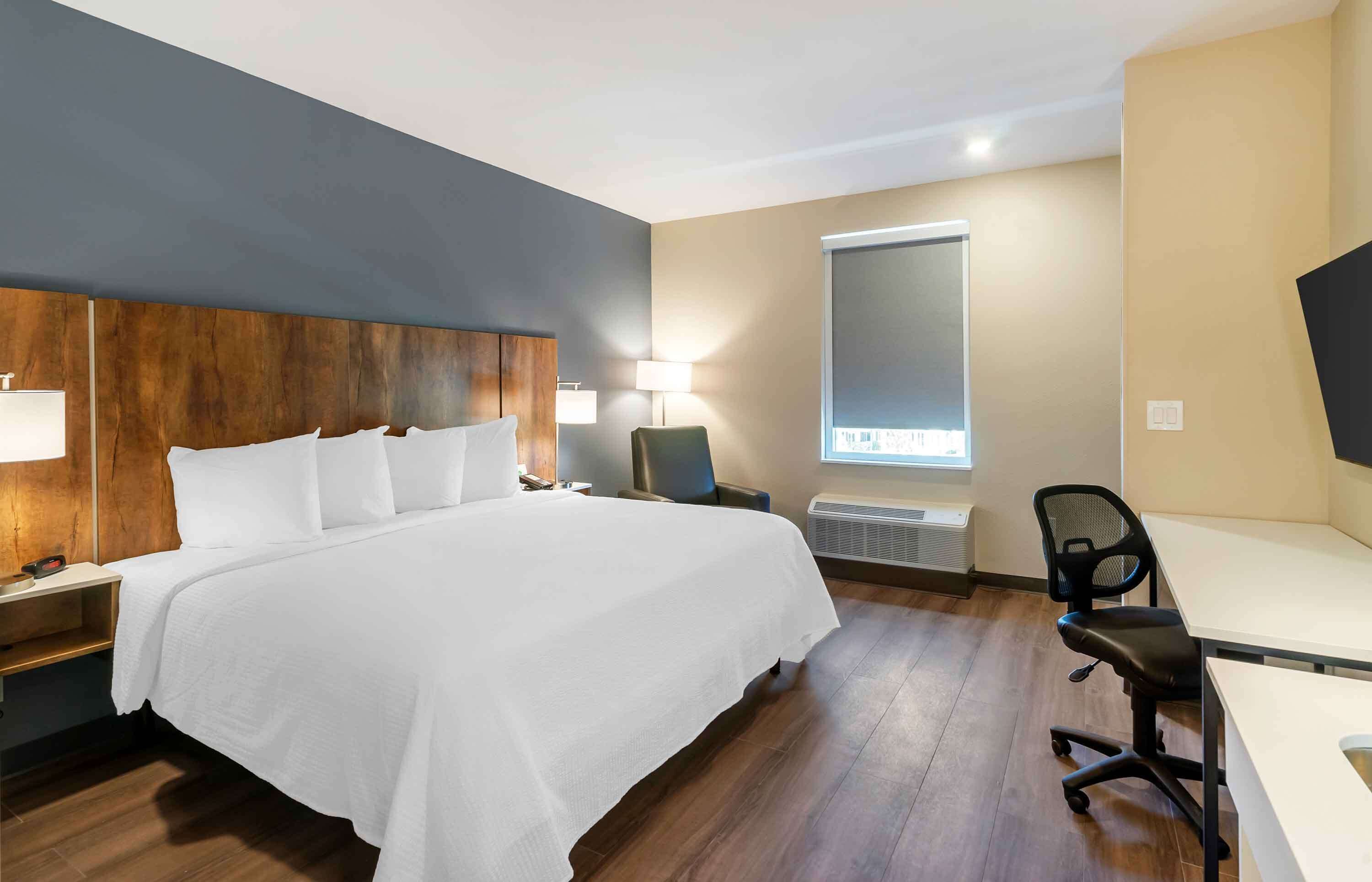 Une chambre d’hôtel avec un grand lit, un bureau, une chaise, une lampe et une fenêtre.