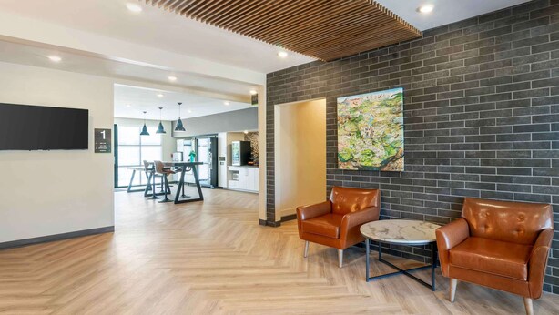 Een moderne hotellobby met een houten vloer, lederen fauteuils, een ronde tafel en een groot abstract schilderij aan de muur.