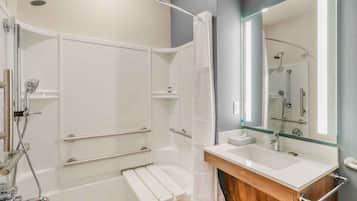 Un baño moderno con ducha a nivel, tocador con cerramiento de vidrio y un espejo grande.
