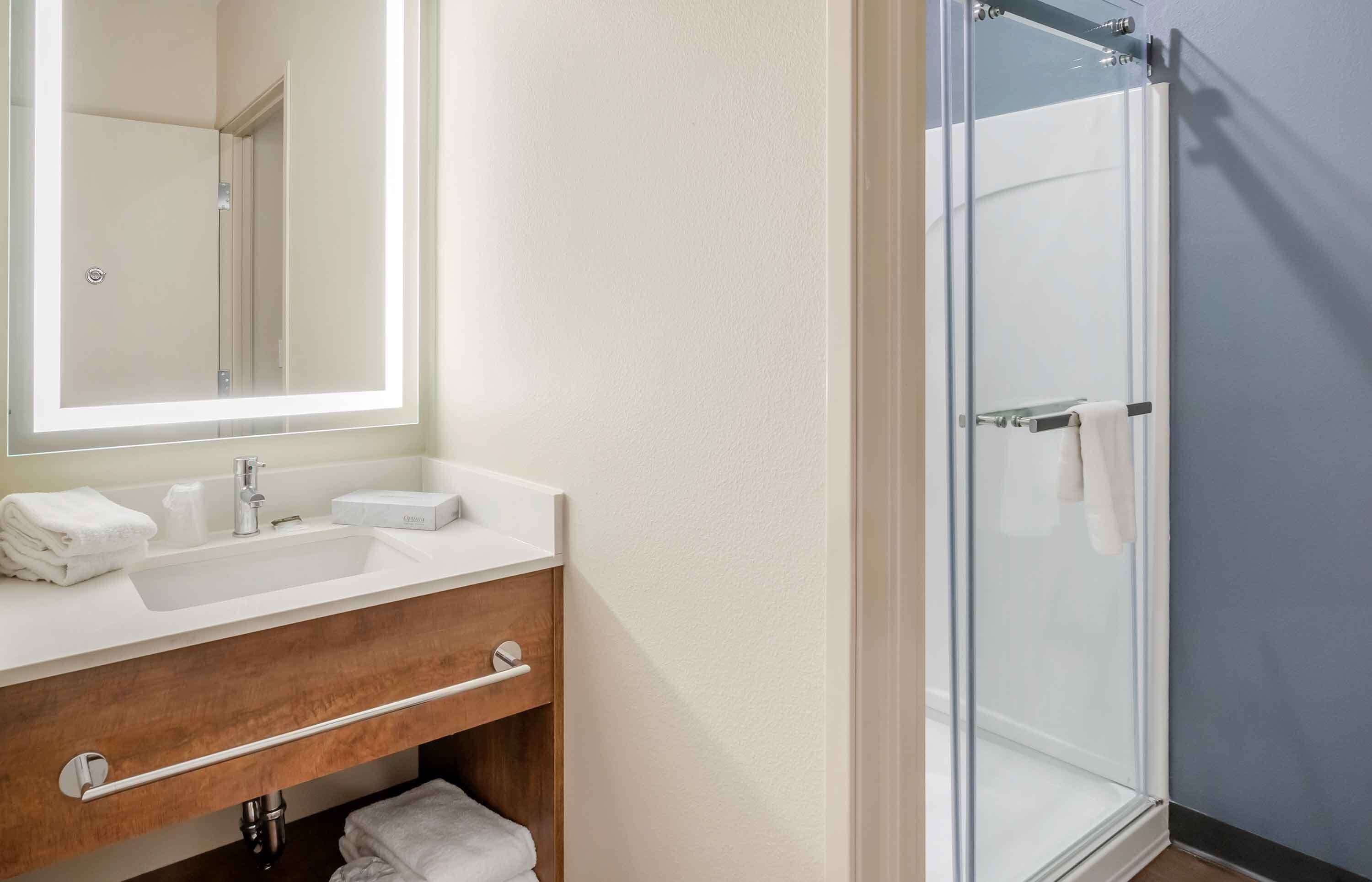Une salle de bain avec un lavabo blanc, un miroir, une cabine de douche en verre et un meuble-lavabo en bois.