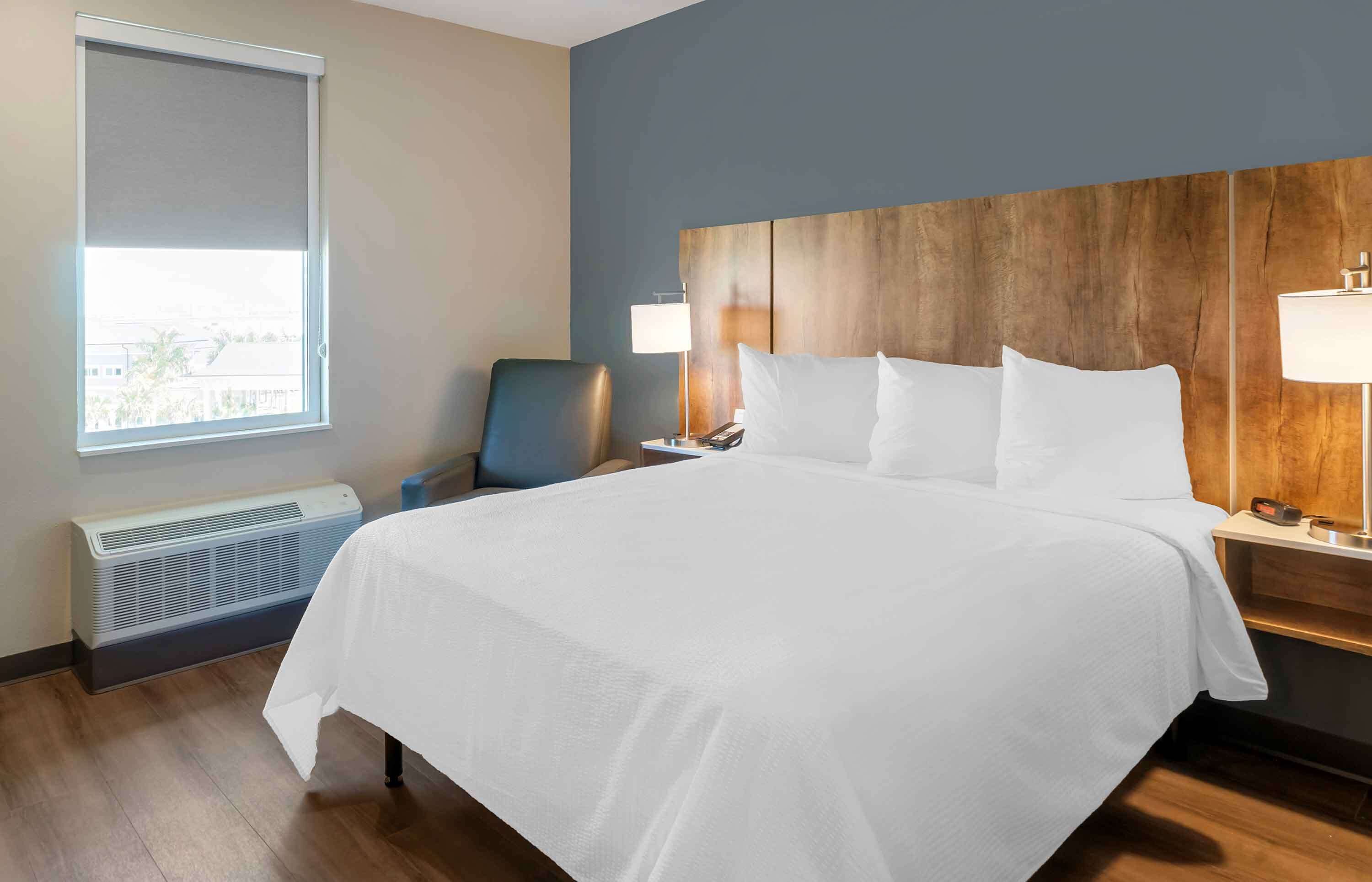 Ein Hotelzimmer mit einem großen Bett, einem Sessel, einem Schreibtisch mit Lampe, einem Heizgerät und einem Fenster mit Blick.