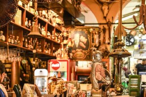 A cluttered shop with various items on shelves and hanging, including a bell, a statue, and a Coca-Cola refrigerator. - Printhouse Boutique STU10 by Sea N' Rent (Haifa)
