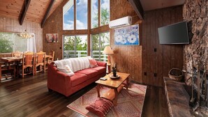 Un salón amplio con sofá rojo, mesa de comedor de madera y grandes ventanales con vistas al exterior.