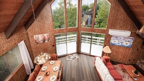 Una habitación acogedora con paredes de madera, ventanas amplias, una mesa de comedor para dos personas y un sofá.